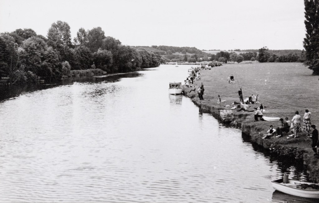 Black and white photograph of groups of visitors lining the Thames riverside at Pangbourne.