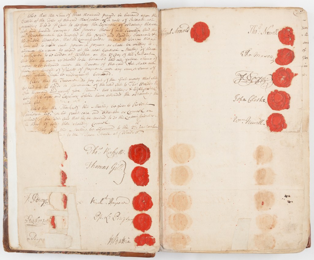 Colour photograph of two pages of a minute book featuring the conclusion of the first meeting of the Thames Navigation Commission with signatures and red seals.