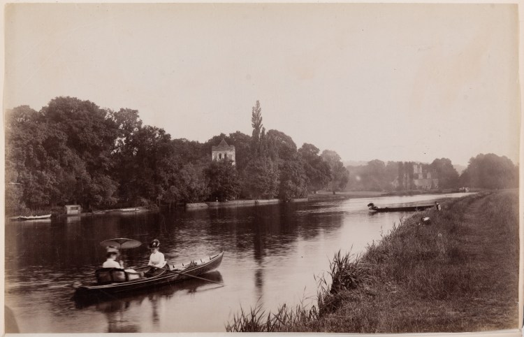 Black and white photograph of two women boating on the river near Bisham Abbey, Bisham Abbey church can be seen in the background.